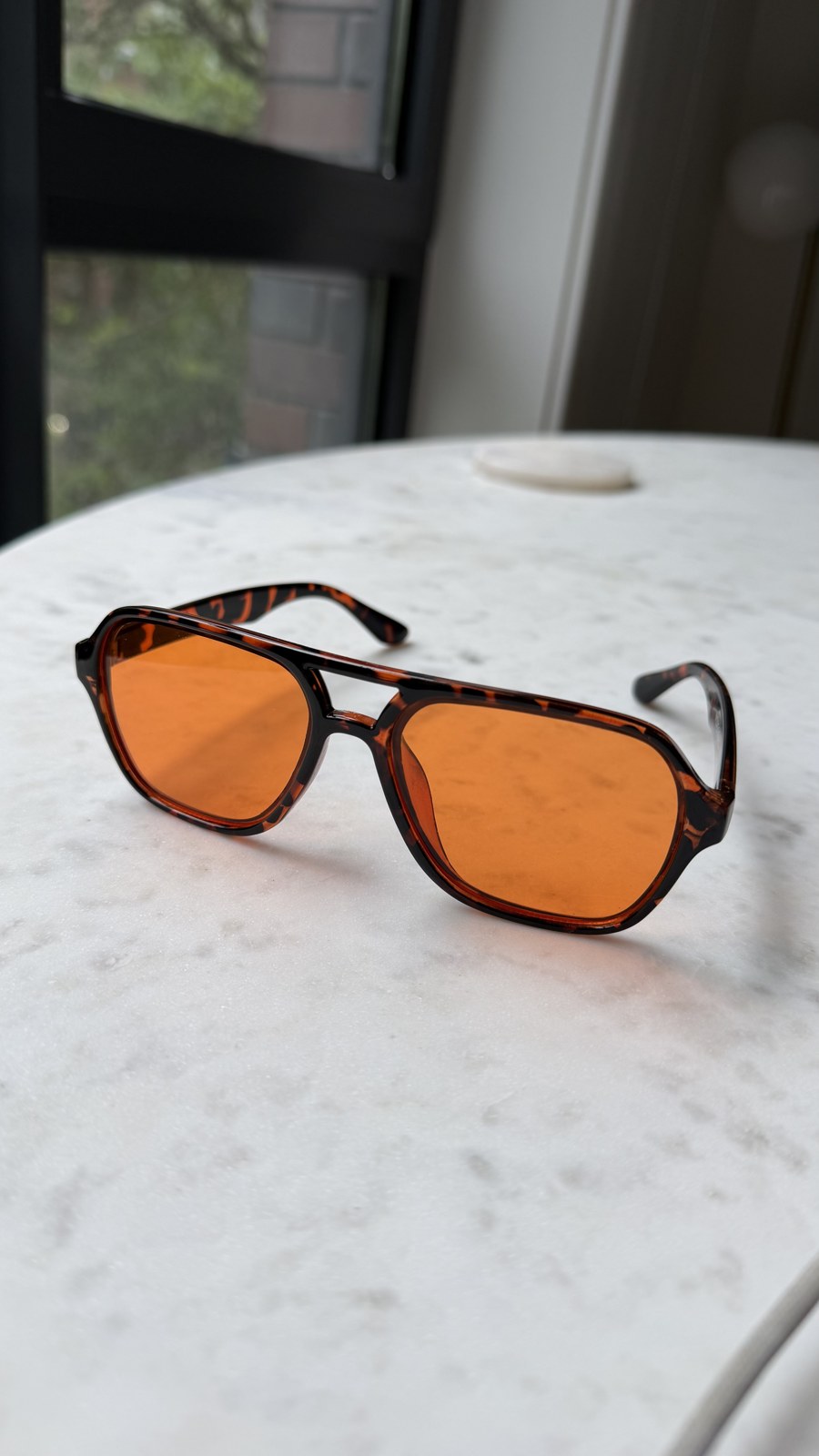 Morning Rave amber tortoise sunglasses resting on a marble table